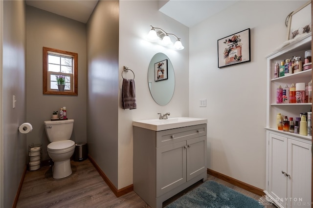 bathroom with toilet, wood finished floors, vanity, and baseboards