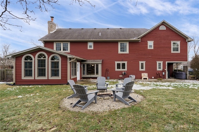 back of property featuring a fire pit, a chimney, fence, and a lawn