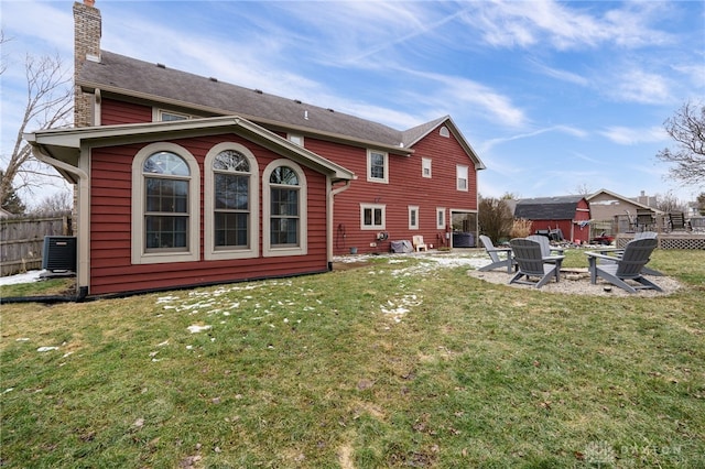 rear view of house with central AC unit, a fire pit, fence, a yard, and a chimney