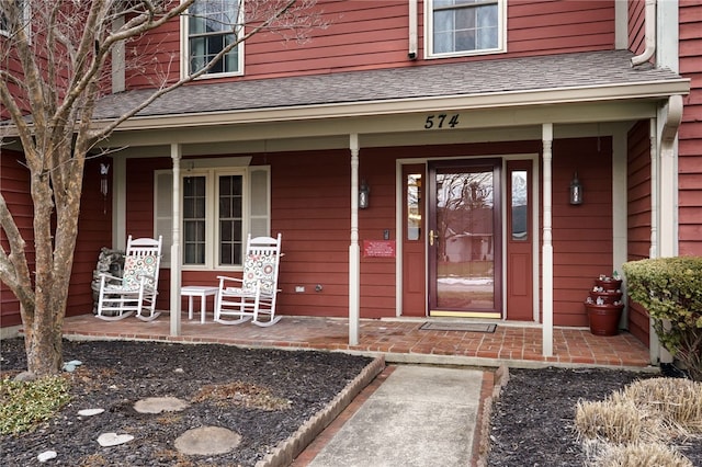 doorway to property featuring a porch and roof with shingles