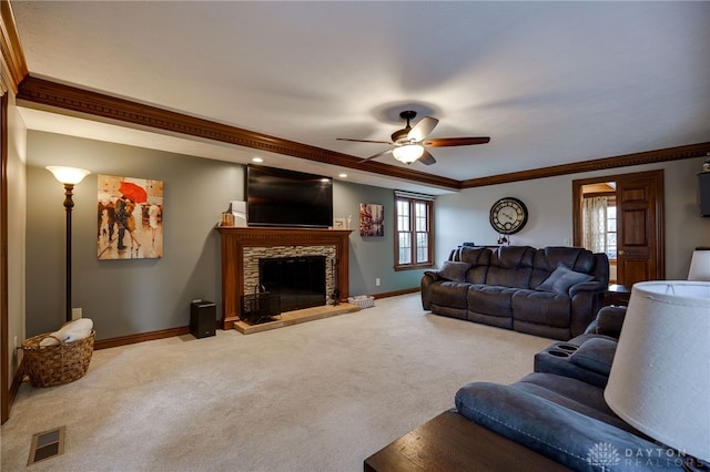 carpeted living area with visible vents, ornamental molding, ceiling fan, a stone fireplace, and baseboards