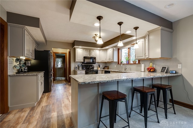 kitchen featuring light wood finished floors, a peninsula, black appliances, a kitchen bar, and a sink