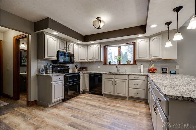 kitchen with light stone counters, a sink, light wood-type flooring, decorative backsplash, and black appliances