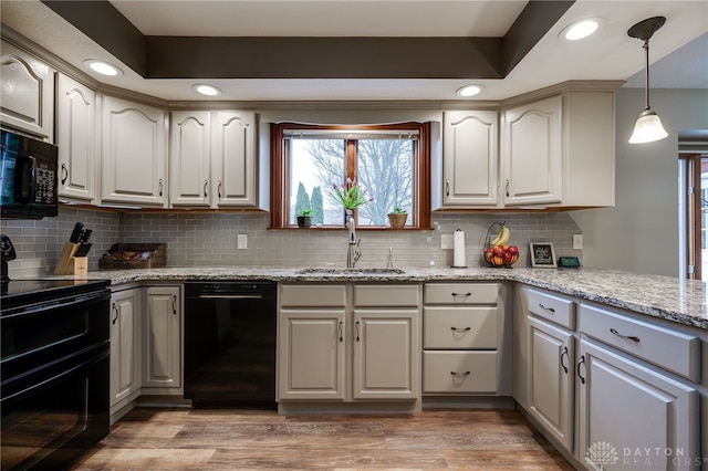 kitchen featuring light wood finished floors, a tray ceiling, black appliances, pendant lighting, and a sink