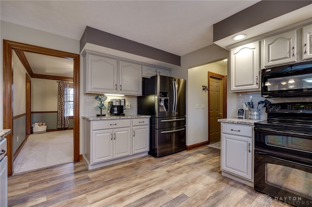 kitchen featuring light wood-style floors, light stone counters, black appliances, and tasteful backsplash