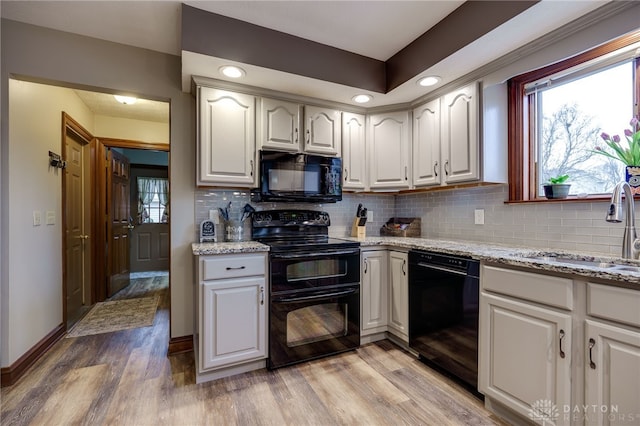 kitchen featuring light stone counters, a sink, light wood-style floors, decorative backsplash, and black appliances