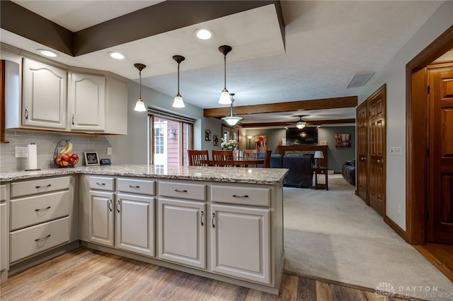 kitchen featuring a peninsula, open floor plan, backsplash, light stone countertops, and pendant lighting