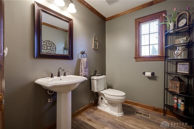 half bathroom featuring baseboards, visible vents, toilet, wood finished floors, and crown molding