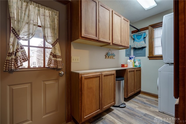 clothes washing area featuring stacked washer and dryer, cabinet space, visible vents, light wood-style floors, and a textured ceiling