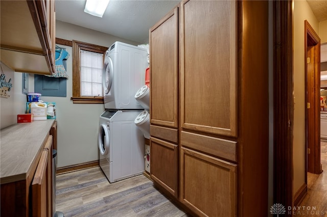 laundry room with cabinet space, light wood-style flooring, and stacked washer and clothes dryer