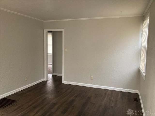 empty room featuring dark wood-style floors, ornamental molding, visible vents, and baseboards