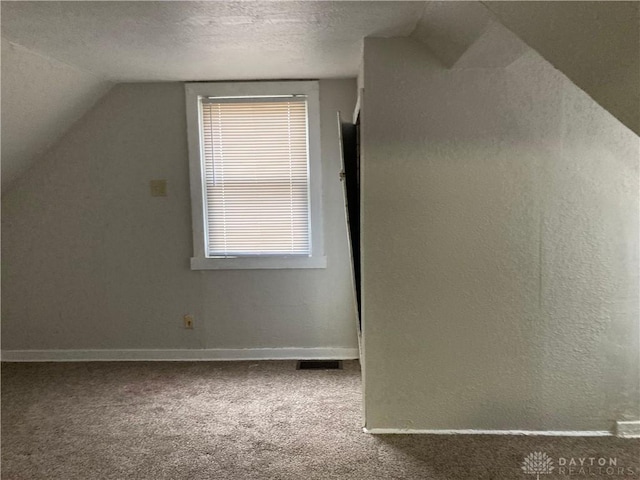 additional living space featuring a textured ceiling, vaulted ceiling, carpet flooring, and baseboards