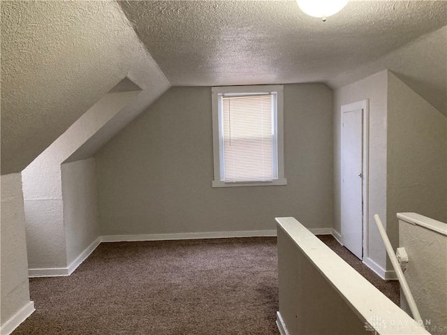 additional living space featuring lofted ceiling, dark colored carpet, a textured ceiling, and baseboards