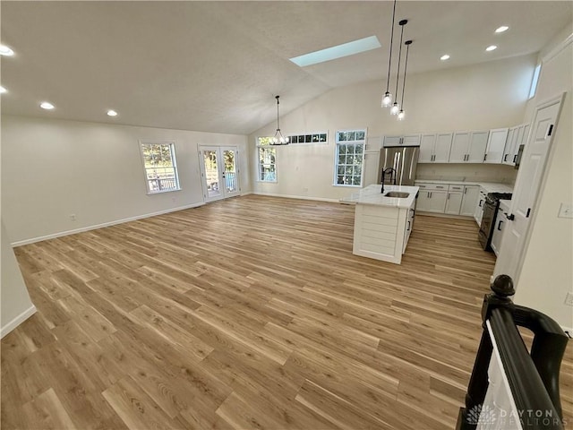 kitchen featuring a skylight, light wood-style flooring, black gas range, open floor plan, and stainless steel fridge with ice dispenser