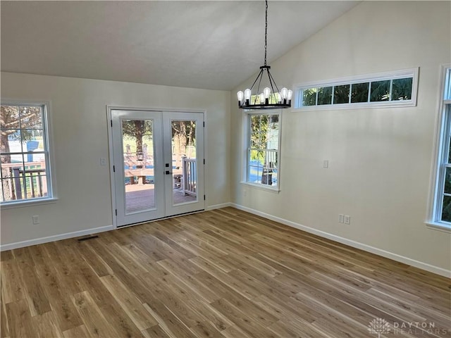 unfurnished dining area featuring lofted ceiling, a chandelier, wood finished floors, visible vents, and baseboards