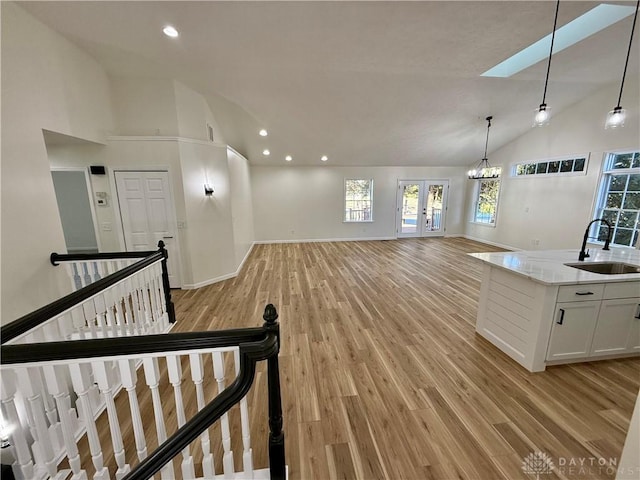 unfurnished living room with high vaulted ceiling, a healthy amount of sunlight, a sink, and light wood finished floors