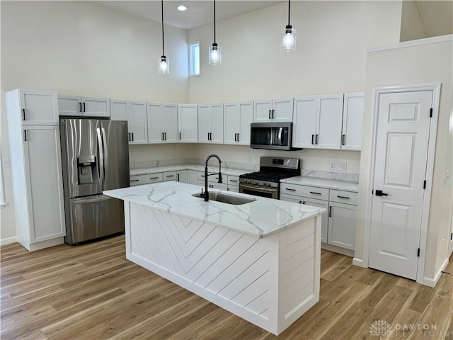 kitchen with light wood-style flooring, appliances with stainless steel finishes, light stone counters, high vaulted ceiling, and a sink