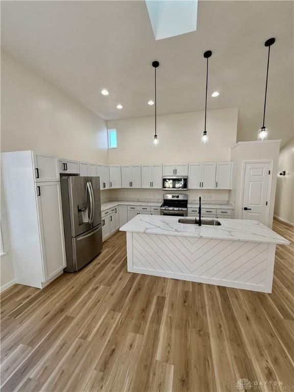 kitchen featuring stainless steel appliances, light wood finished floors, a sink, and white cabinetry