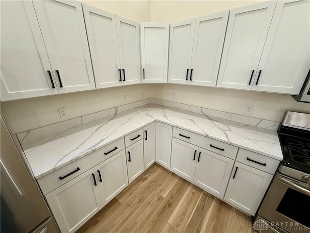 kitchen with light stone counters, stainless steel gas range, light wood-type flooring, and white cabinets