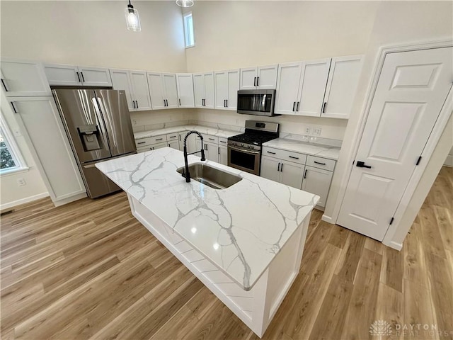 kitchen featuring light wood finished floors, light stone countertops, a high ceiling, stainless steel appliances, and a sink