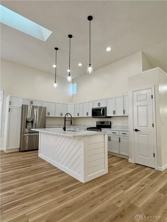 kitchen featuring light wood finished floors, white cabinets, decorative light fixtures, stainless steel appliances, and a sink