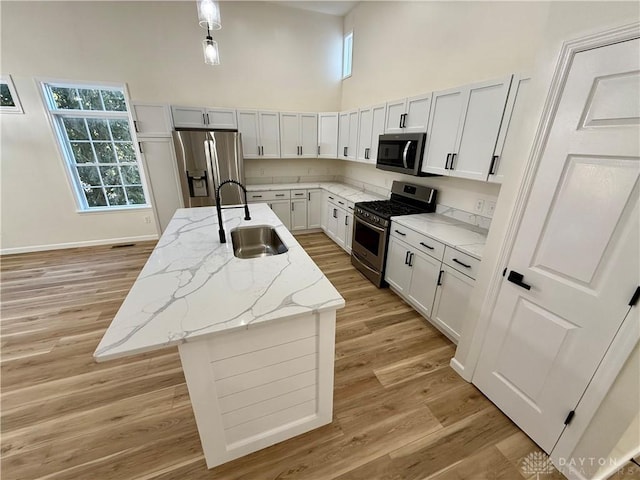 kitchen with light wood-style flooring, a high ceiling, appliances with stainless steel finishes, a sink, and an island with sink