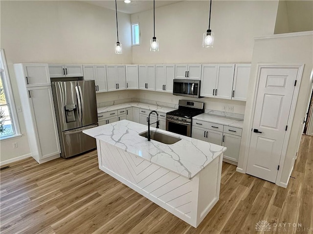 kitchen with a towering ceiling, light wood-style flooring, appliances with stainless steel finishes, hanging light fixtures, and a sink