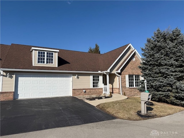 view of front facade featuring a shingled roof, brick siding, driveway, and an attached garage