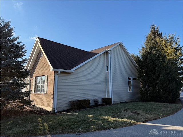 view of side of property featuring roof with shingles, a lawn, and brick siding