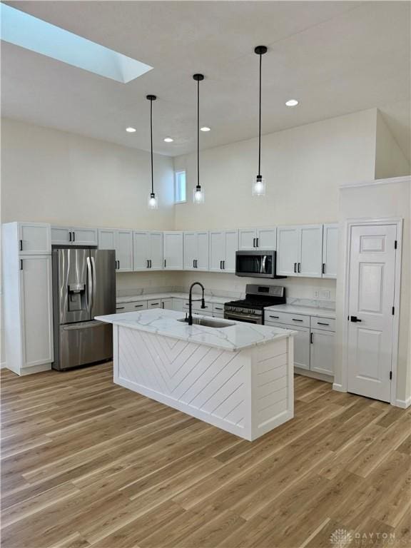 kitchen with stainless steel appliances, a towering ceiling, light wood-style flooring, a sink, and light stone countertops