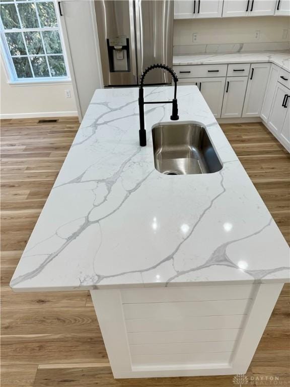 kitchen with light stone counters, light wood-style flooring, white cabinetry, a sink, and stainless steel fridge