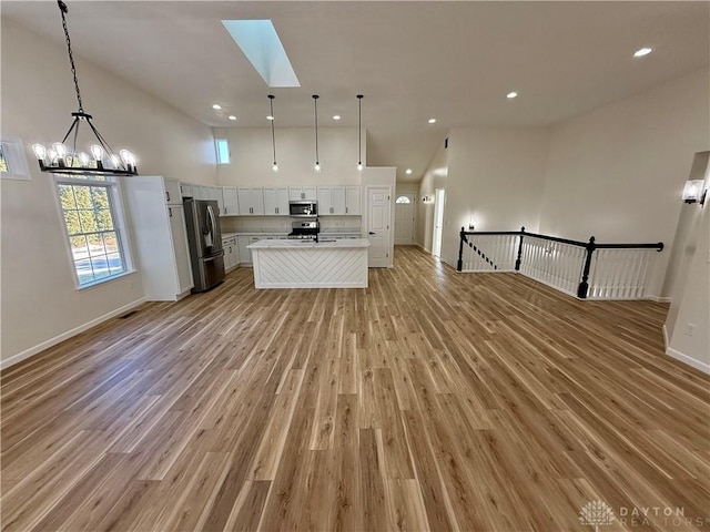 kitchen featuring stainless steel appliances, a high ceiling, light wood-style floors, open floor plan, and white cabinets