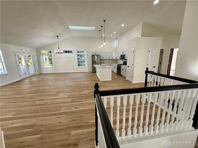 interior space with a skylight, baseboards, wood finished floors, french doors, and high vaulted ceiling