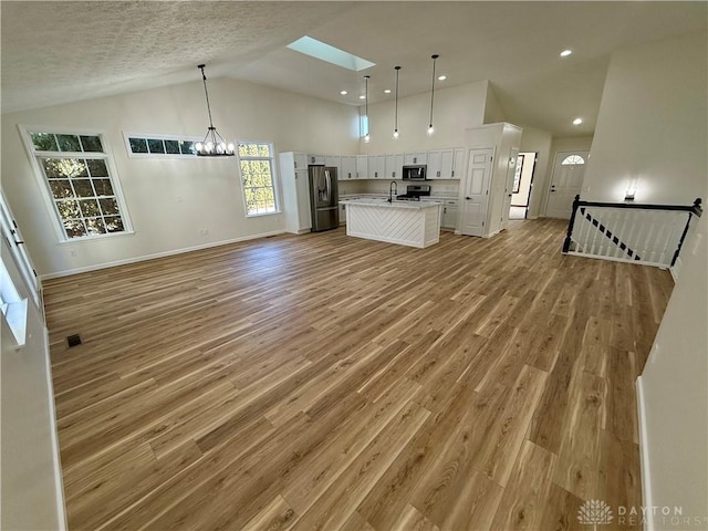 kitchen with a center island with sink, appliances with stainless steel finishes, open floor plan, white cabinetry, and light wood-type flooring