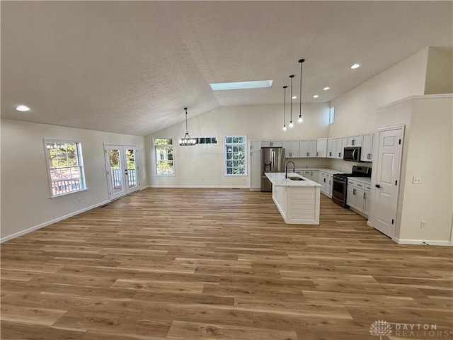 kitchen with a skylight, a sink, white cabinets, open floor plan, and appliances with stainless steel finishes