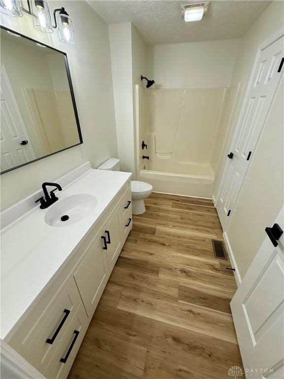 bathroom featuring shower / washtub combination, toilet, a textured ceiling, vanity, and wood finished floors