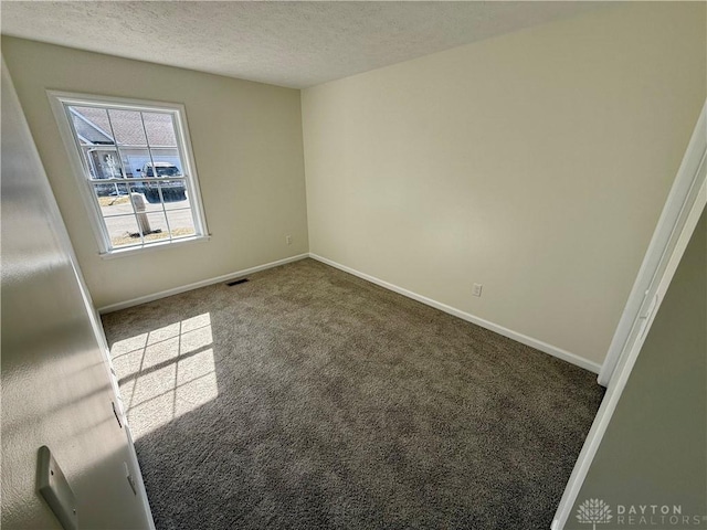 spare room with carpet floors, visible vents, a textured ceiling, and baseboards