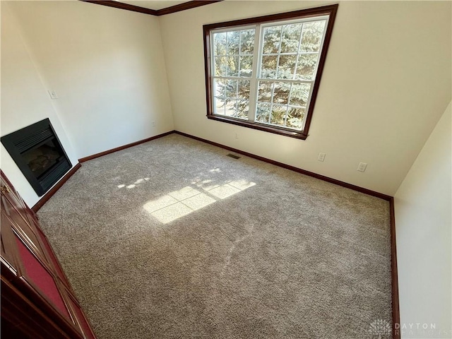 empty room with carpet floors, a glass covered fireplace, visible vents, and baseboards