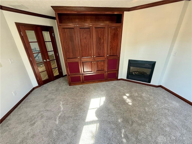 unfurnished bedroom with baseboards, french doors, crown molding, and a glass covered fireplace