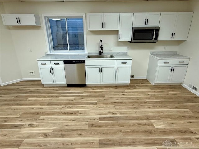 kitchen with a sink, visible vents, white cabinets, appliances with stainless steel finishes, and light wood-type flooring