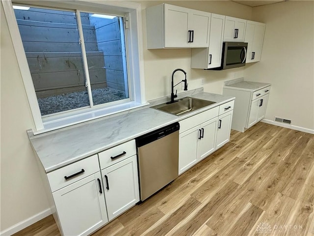 kitchen with light wood finished floors, visible vents, white cabinets, stainless steel appliances, and a sink