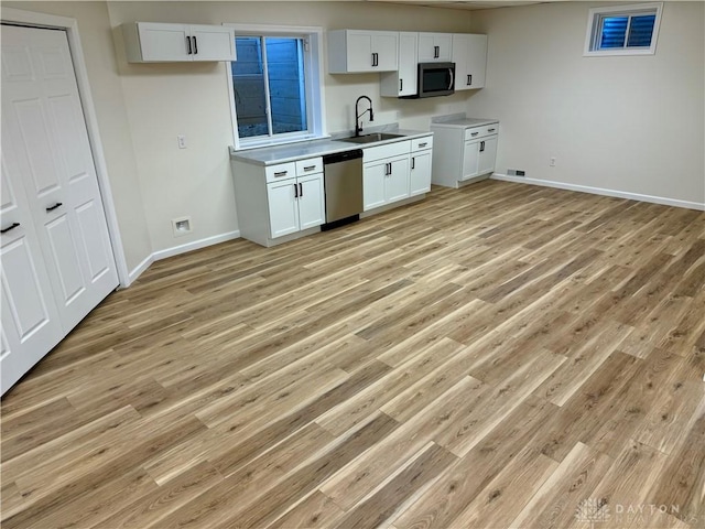 kitchen with baseboards, appliances with stainless steel finishes, a sink, and white cabinets