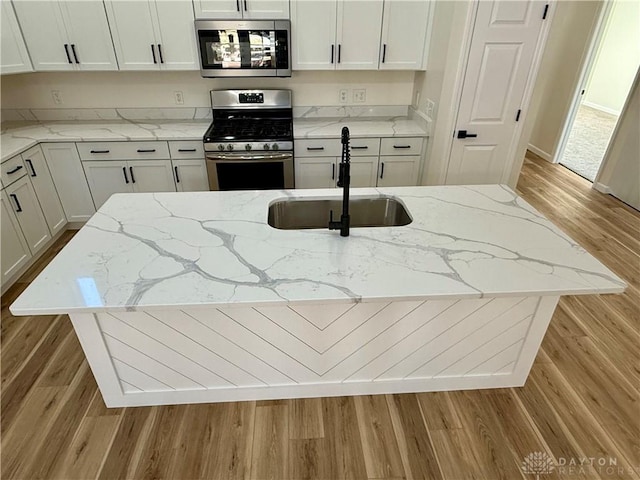 kitchen with wood finished floors, appliances with stainless steel finishes, white cabinets, a sink, and light stone countertops