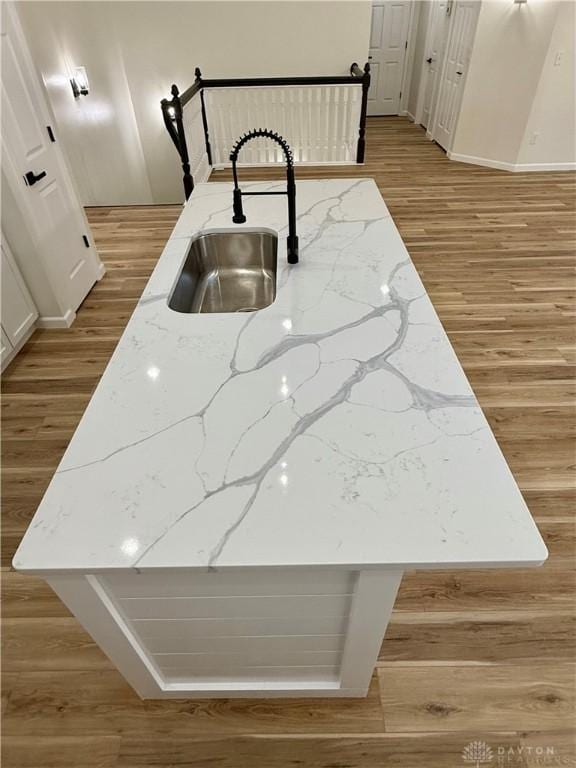 kitchen featuring light stone counters, a sink, and wood finished floors