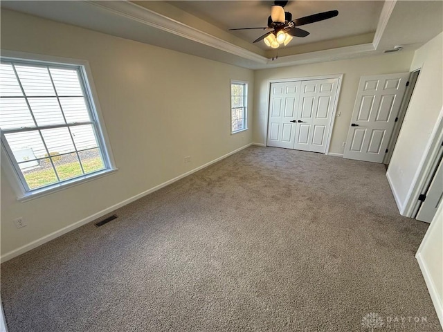 unfurnished bedroom with a tray ceiling, a closet, visible vents, carpet flooring, and baseboards