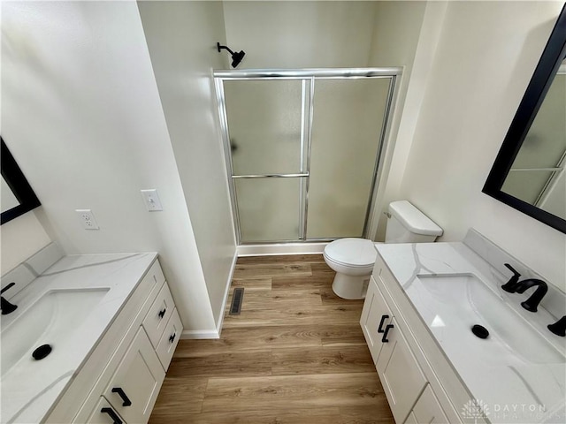 bathroom featuring a stall shower, toilet, two vanities, wood finished floors, and a sink