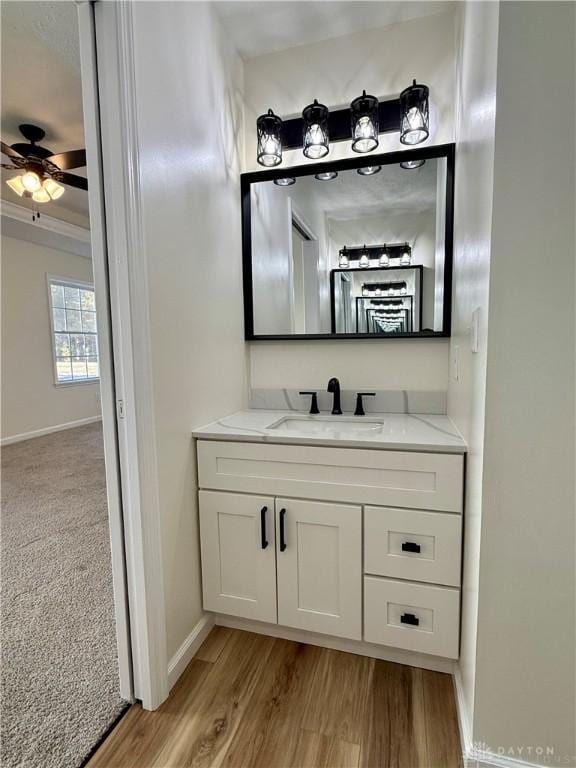 bathroom with a ceiling fan, vanity, baseboards, and wood finished floors