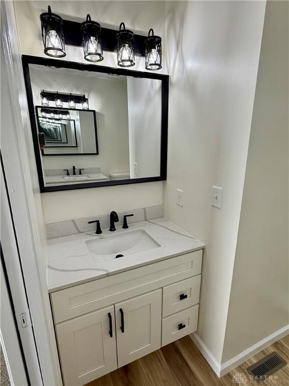 half bath with visible vents, vanity, baseboards, and wood finished floors