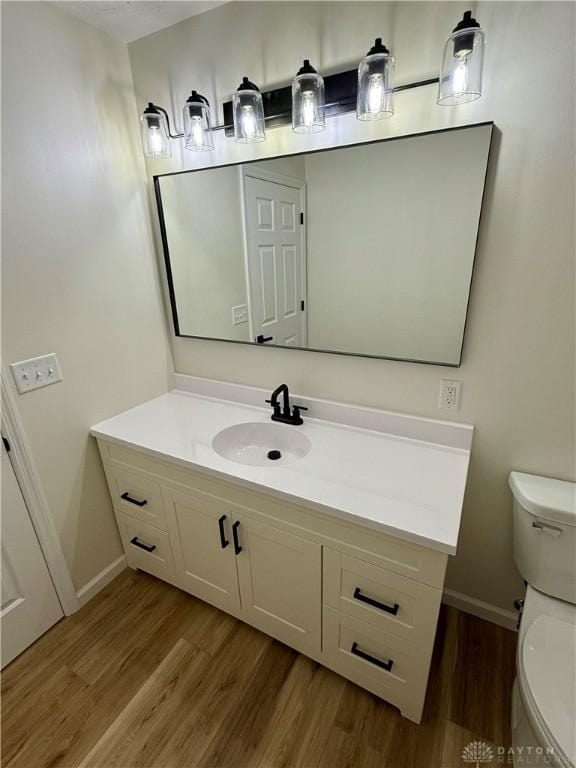 half bath featuring toilet, baseboards, wood finished floors, and vanity