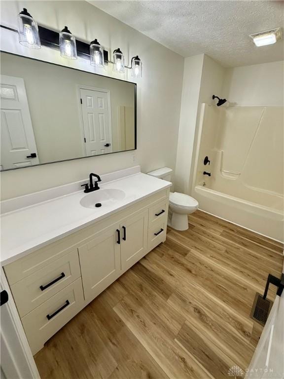 full bath featuring bathing tub / shower combination, toilet, wood finished floors, a textured ceiling, and vanity